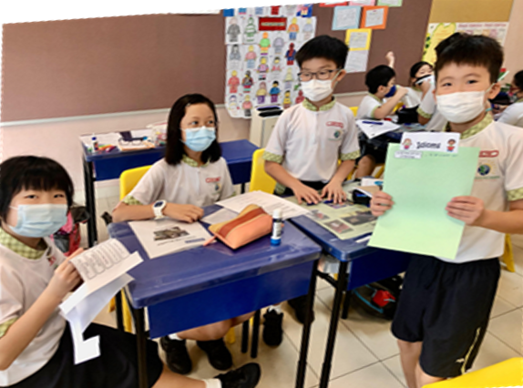 Four young students in uniforms and face masks hold papers in a colorful classroom.